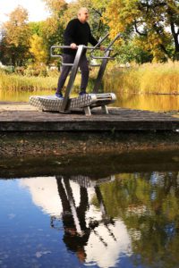 An elderly man exercises on the GreenMill City outdoor treadmill in the park on a footbridge