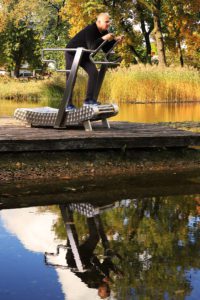 A middle-aged man walks on the Green Mill City outdoor treadmill by the water