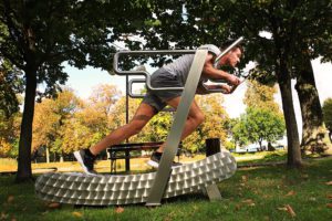 A man is exercising on the GreenMill City outdoor treadmill in the park, his body is bent forward